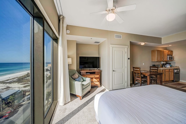 bedroom featuring light carpet, a view of the beach, a water view, and ceiling fan