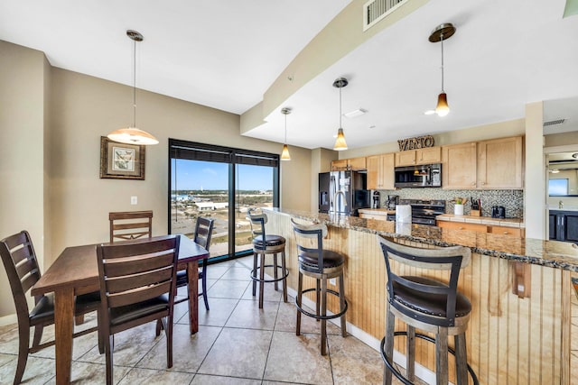 kitchen featuring decorative backsplash, a kitchen bar, stainless steel appliances, decorative light fixtures, and dark stone countertops