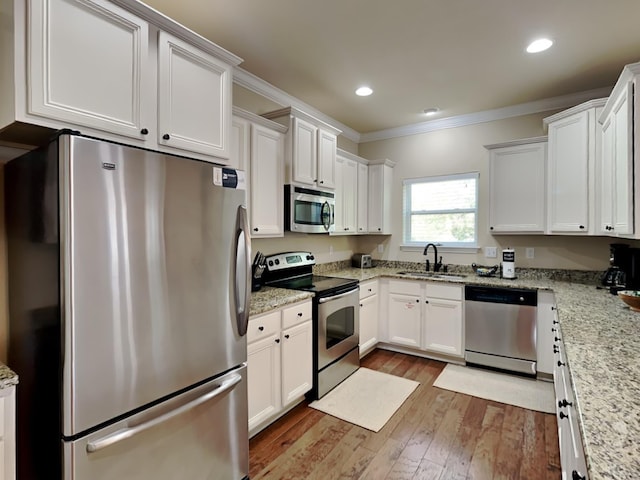 kitchen with appliances with stainless steel finishes, light stone counters, crown molding, sink, and white cabinetry