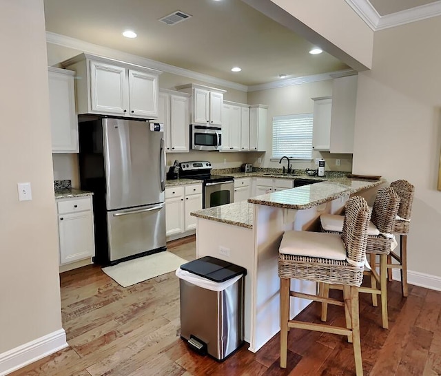 kitchen with white cabinetry, light stone countertops, kitchen peninsula, a kitchen bar, and appliances with stainless steel finishes