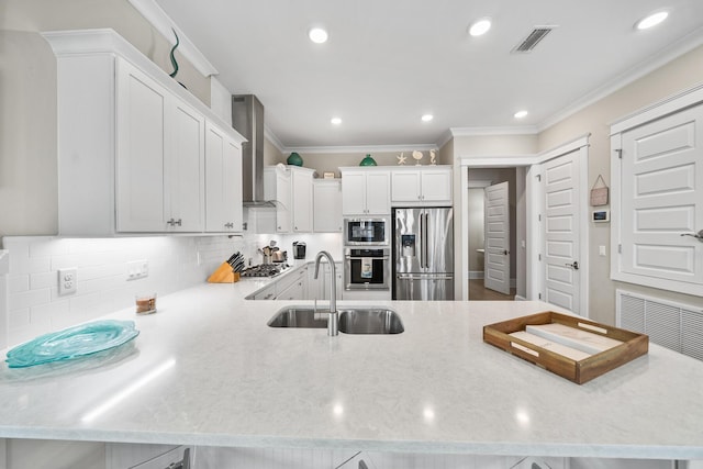 kitchen featuring white cabinetry, sink, wall chimney exhaust hood, stainless steel appliances, and kitchen peninsula