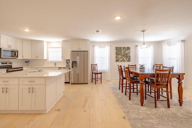 kitchen featuring pendant lighting, white cabinets, light wood-type flooring, and appliances with stainless steel finishes