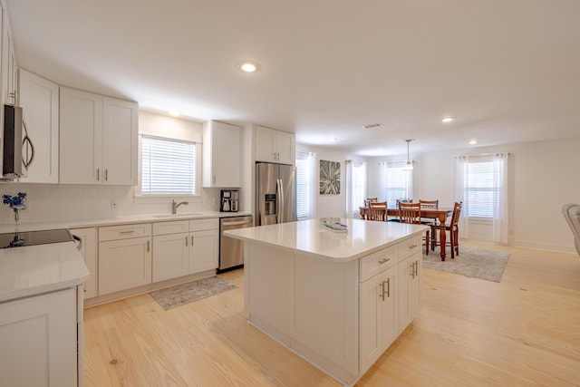 kitchen featuring a center island, sink, decorative light fixtures, white cabinetry, and stainless steel appliances