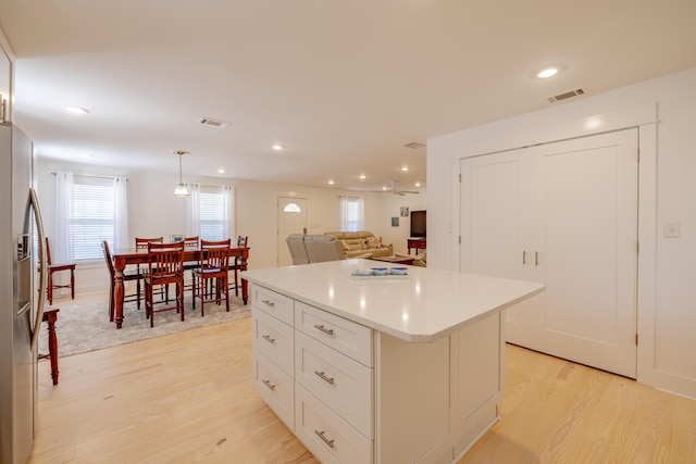 kitchen with decorative light fixtures, white cabinets, stainless steel fridge with ice dispenser, light hardwood / wood-style floors, and a kitchen island