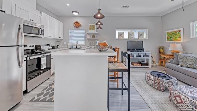 kitchen with hanging light fixtures, sink, a breakfast bar area, white cabinetry, and stainless steel appliances