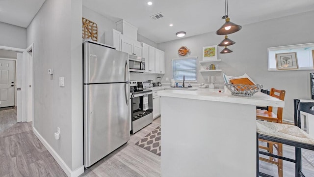 kitchen with white cabinets, decorative light fixtures, stainless steel appliances, and light hardwood / wood-style flooring