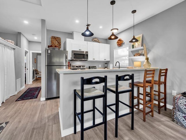 kitchen featuring white cabinets, a kitchen bar, pendant lighting, and stainless steel appliances