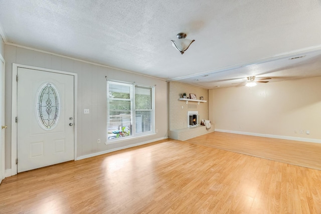 unfurnished living room with crown molding, light hardwood / wood-style flooring, ceiling fan, a textured ceiling, and a fireplace