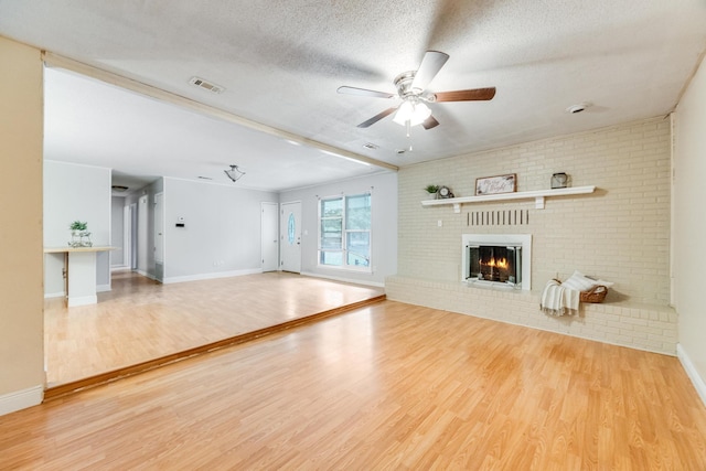 unfurnished living room featuring hardwood / wood-style floors, ceiling fan, a fireplace, a textured ceiling, and brick wall