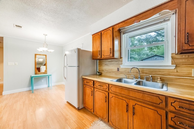 kitchen featuring an inviting chandelier, white refrigerator, sink, hanging light fixtures, and tasteful backsplash