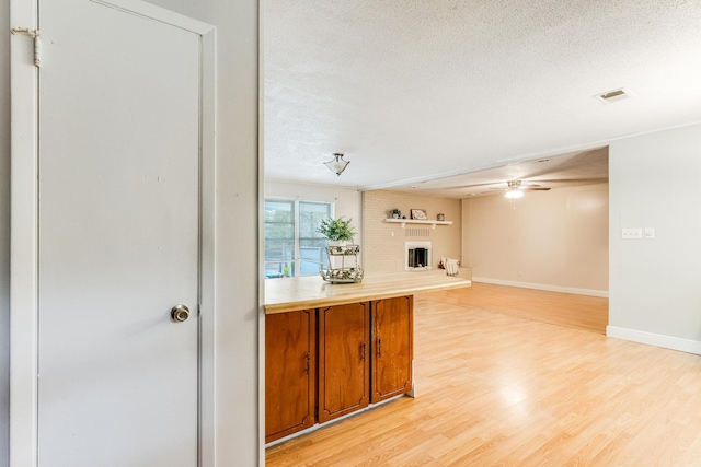 interior space with a fireplace, a textured ceiling, light hardwood / wood-style floors, and ceiling fan