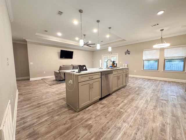 kitchen featuring gray cabinetry, a center island with sink, stainless steel dishwasher, a tray ceiling, and decorative light fixtures