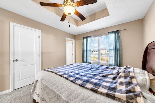 carpeted bedroom with a raised ceiling and ceiling fan