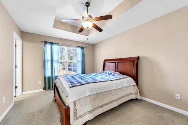 bedroom featuring light carpet, a textured ceiling, a tray ceiling, and ceiling fan