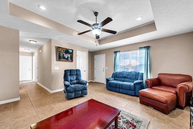 tiled living room featuring ceiling fan, a textured ceiling, and a tray ceiling