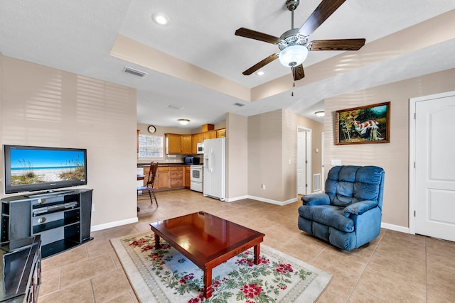 tiled living room featuring a raised ceiling, ceiling fan, and a textured ceiling