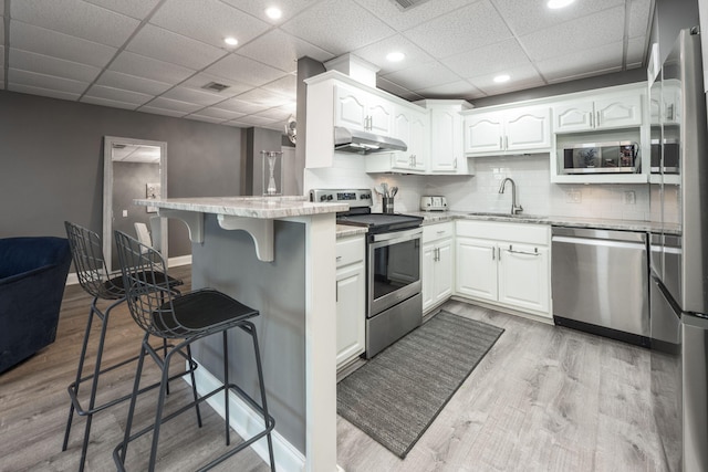 kitchen with a kitchen bar, kitchen peninsula, white cabinets, and appliances with stainless steel finishes