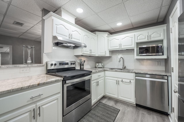 kitchen featuring appliances with stainless steel finishes, a drop ceiling, sink, light hardwood / wood-style flooring, and white cabinetry