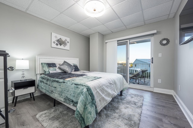 bedroom with dark hardwood / wood-style flooring, access to outside, and a paneled ceiling