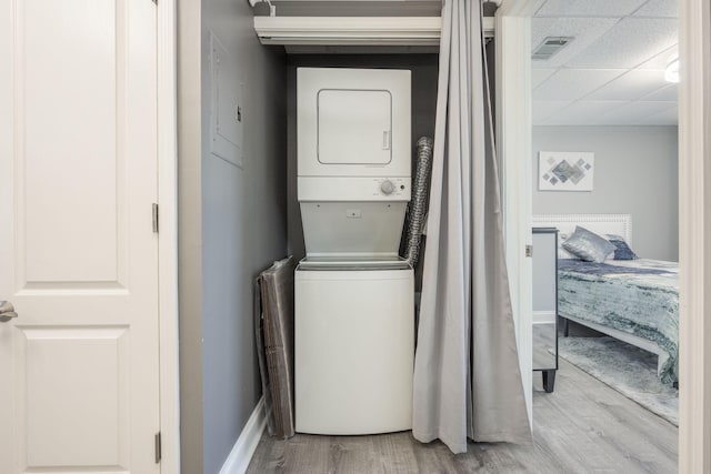 clothes washing area with light hardwood / wood-style flooring and stacked washer / drying machine