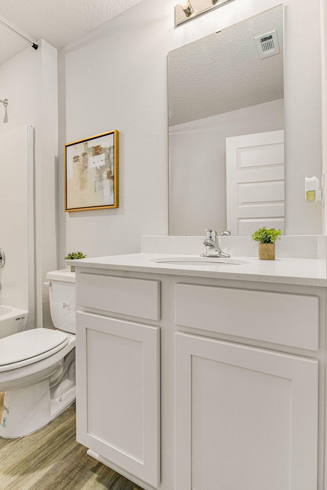 full bathroom with hardwood / wood-style floors, vanity, shower / bathing tub combination, toilet, and a textured ceiling