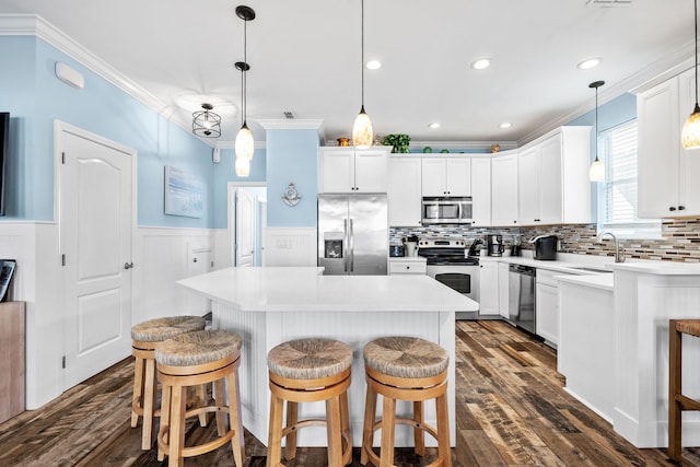 kitchen with a wainscoted wall, stainless steel appliances, a sink, a center island, and crown molding