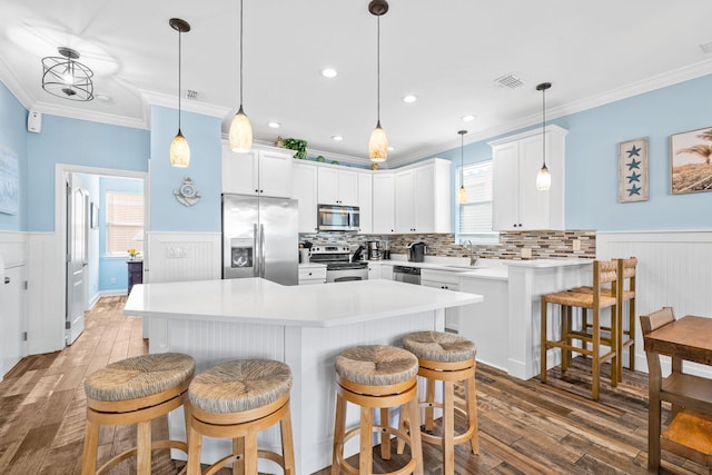 kitchen featuring visible vents, stainless steel appliances, a breakfast bar area, and wainscoting