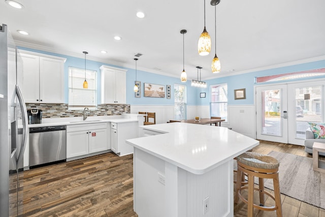 kitchen with stainless steel appliances, dark wood-type flooring, wainscoting, a center island, and crown molding