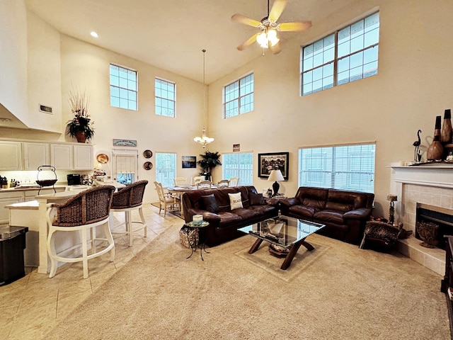 tiled living room featuring a tile fireplace, a high ceiling, and ceiling fan with notable chandelier