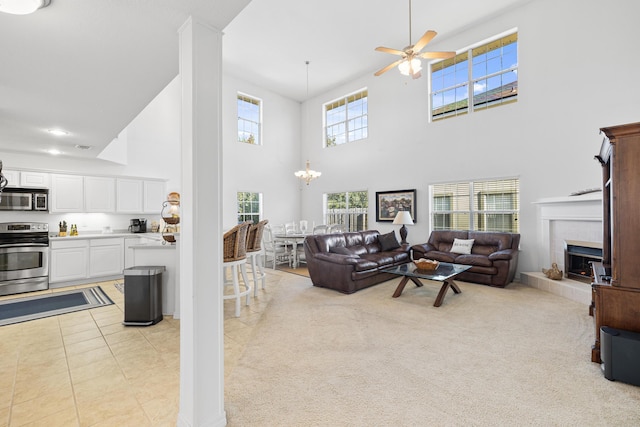 carpeted living room featuring a high ceiling, ceiling fan with notable chandelier, and a tiled fireplace