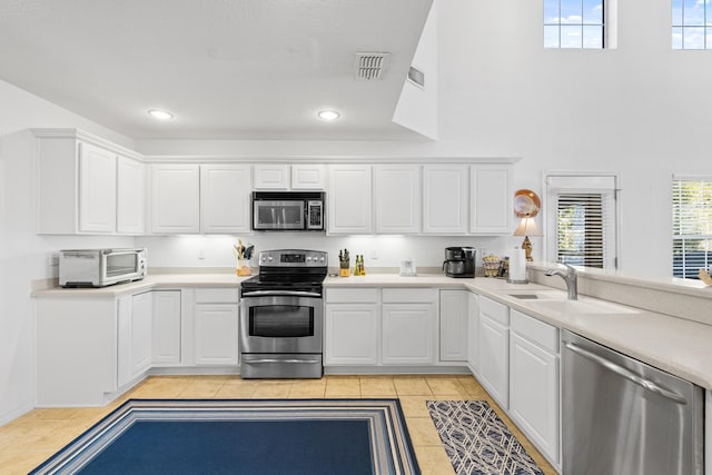 kitchen with light tile patterned floors, sink, stainless steel appliances, and white cabinetry