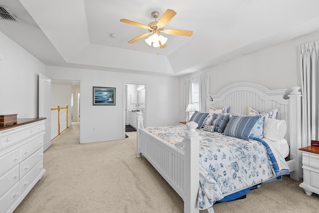 carpeted bedroom with ceiling fan, ensuite bathroom, and a raised ceiling