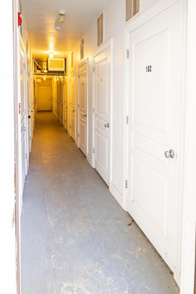 hall featuring concrete flooring, a wall mounted AC, and visible vents