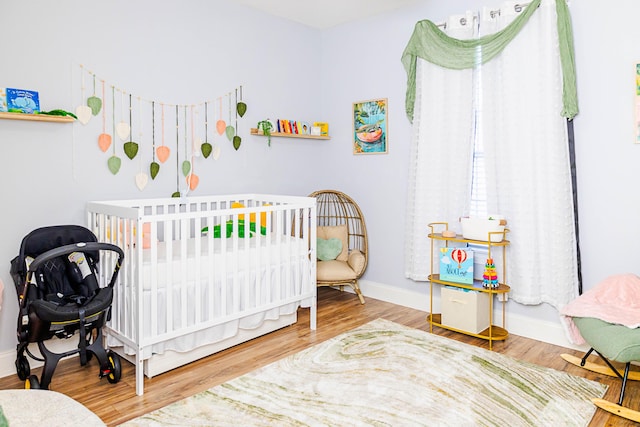 bedroom featuring a crib, baseboards, and wood finished floors