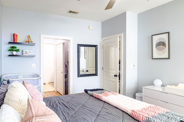 bedroom featuring a ceiling fan, a textured ceiling, visible vents, and wood finished floors