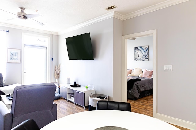 living room featuring visible vents, baseboards, a ceiling fan, ornamental molding, and light wood-type flooring