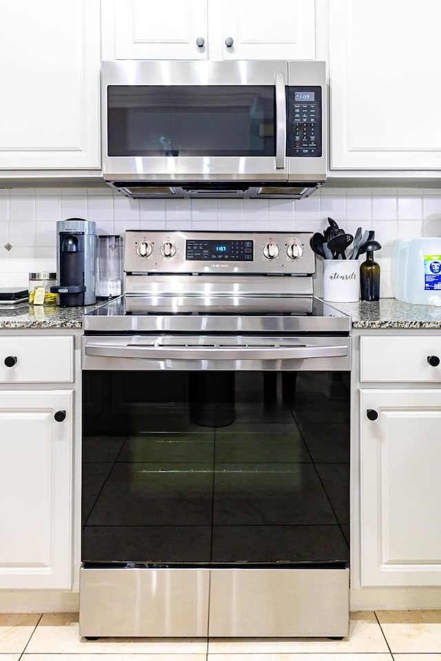 kitchen with white cabinets, light stone countertops, stainless steel appliances, and decorative backsplash