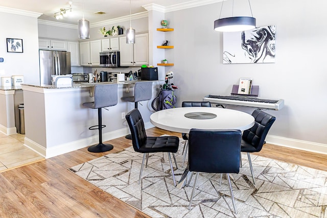 dining room featuring baseboards, light wood-style floors, track lighting, and crown molding