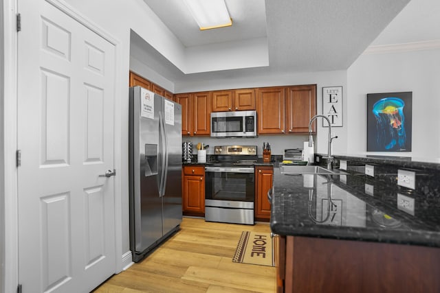 kitchen with appliances with stainless steel finishes, light wood-type flooring, ornamental molding, sink, and dark stone countertops