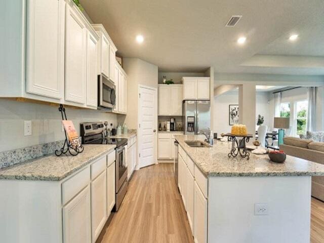 kitchen with white cabinetry, sink, light hardwood / wood-style flooring, a center island with sink, and appliances with stainless steel finishes