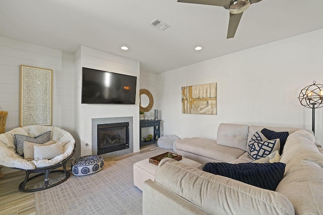 living room featuring a large fireplace, light hardwood / wood-style flooring, and ceiling fan