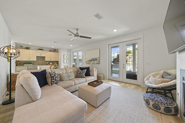 living room with french doors, light hardwood / wood-style flooring, and ceiling fan with notable chandelier