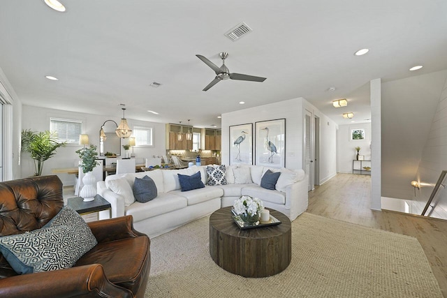 living room featuring ceiling fan with notable chandelier and light hardwood / wood-style floors