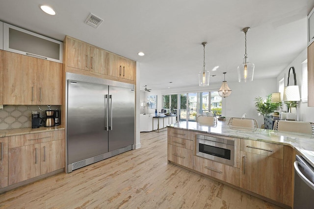 kitchen featuring tasteful backsplash, light stone counters, pendant lighting, built in appliances, and light brown cabinets