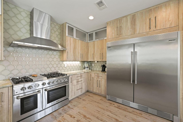 kitchen featuring decorative backsplash, wall chimney exhaust hood, light brown cabinets, light hardwood / wood-style flooring, and high quality appliances