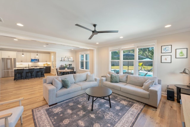 living room with ceiling fan, sink, light wood-type flooring, and crown molding