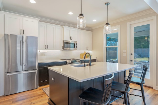 kitchen featuring appliances with stainless steel finishes, a kitchen island with sink, decorative light fixtures, light hardwood / wood-style flooring, and white cabinetry