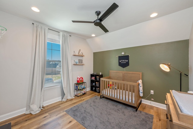 bedroom with hardwood / wood-style flooring, ceiling fan, lofted ceiling, and a nursery area