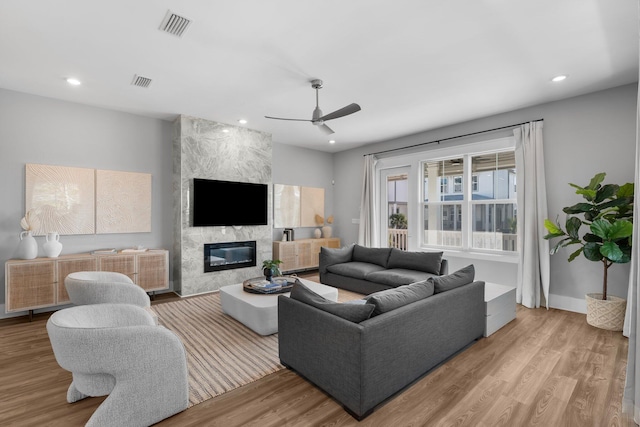 living room featuring ceiling fan, a fireplace, and light hardwood / wood-style flooring