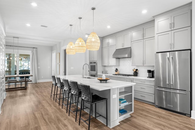 kitchen featuring appliances with stainless steel finishes, decorative light fixtures, a kitchen island with sink, and gray cabinetry